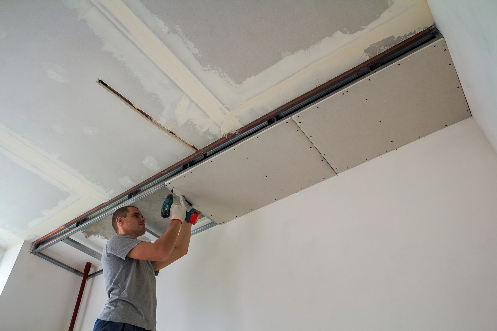 Construction worker assemble a suspended ceiling with drywall and fixing the drywall to the ceiling